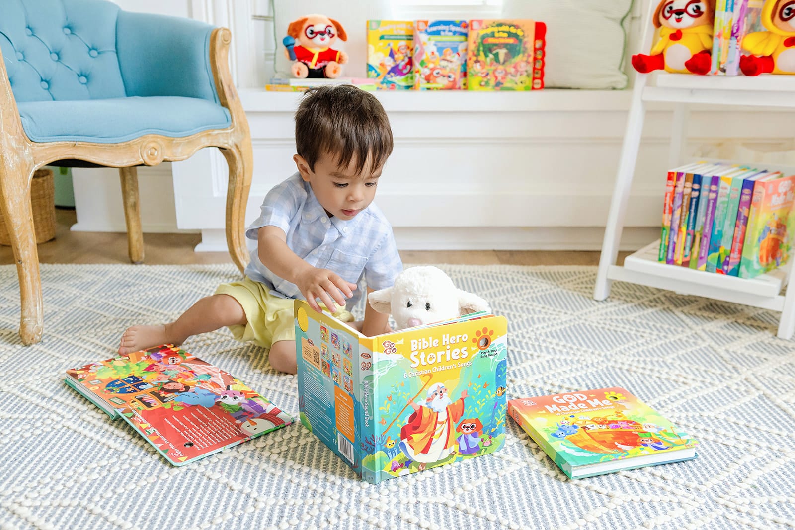 A toddler happily reaching into an open Go Go Bible Hero Stories sound book, surrounded by a full shelf of Go Go Christian sound books — no screen in sight