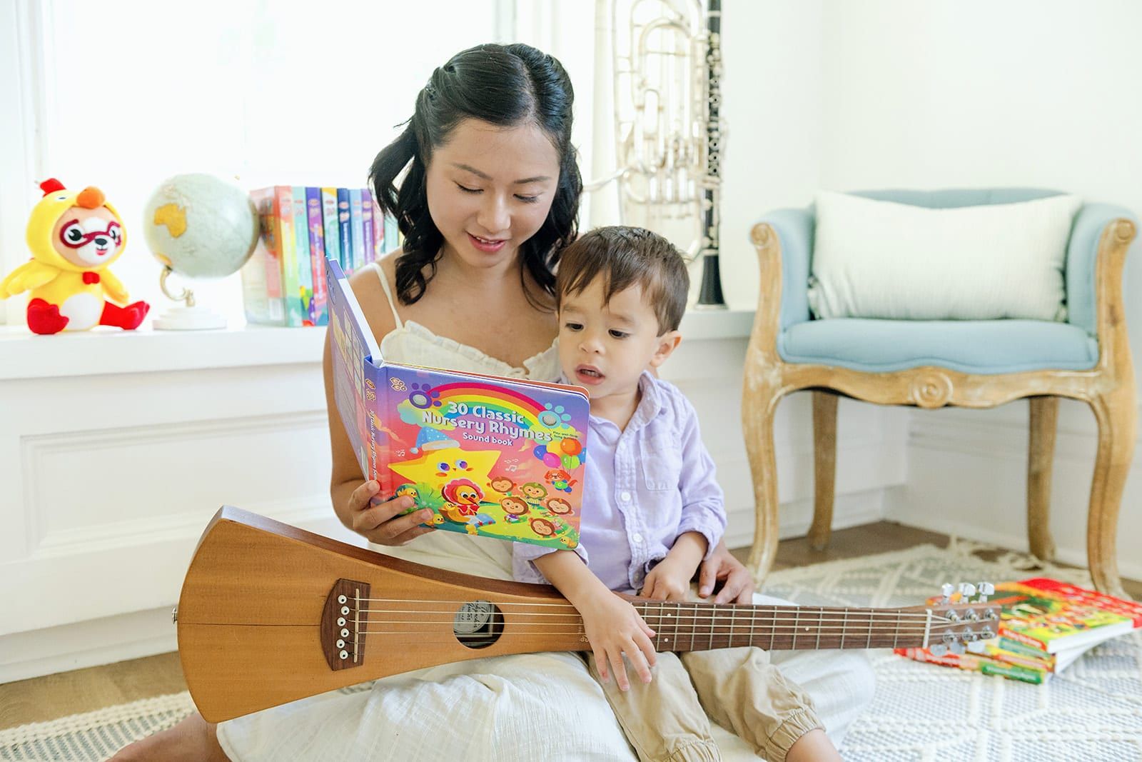 Mom reading the Go Go 30 Classic Nursery Rhymes sound book with her toddler, guitar on her lap
