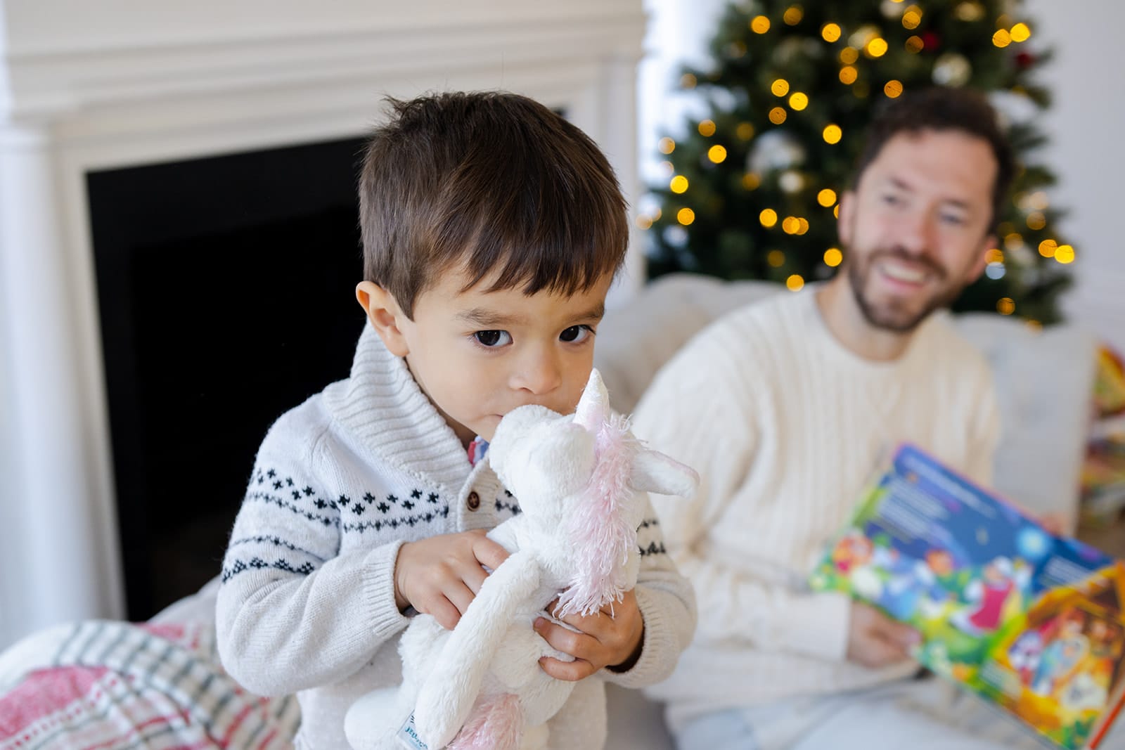 Little boy hugging a soft white Go Go plush toy while his smiling dad holds a book